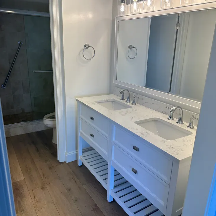 Remodeled bathroom with white double-vanity, marble counter, and tiled walk-in shower