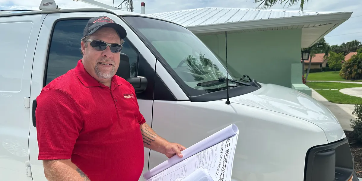 Geoff Worthington standing in front of his white Worthington Construction work van, holding a set of renovation blueprints