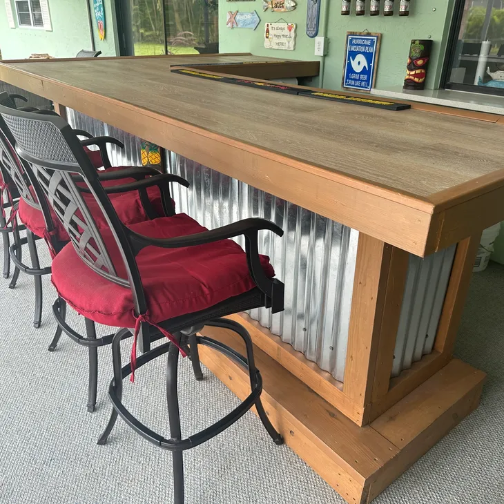 Custom-built outdoor pool bar with wood top, corrugated metal base, and red cushioned chairs