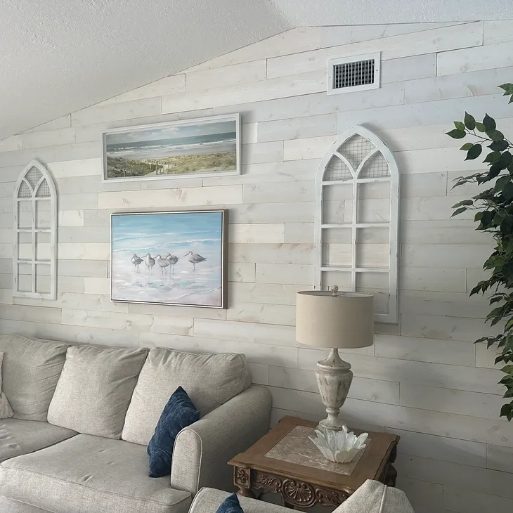 Whitewashed shiplap feature wall in a coastal-styled living room with beach art and a neutral sectional